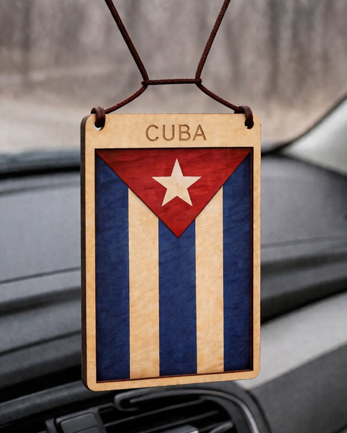 Car ornament with Cuba flag design hanging from a car's rearview mirror.